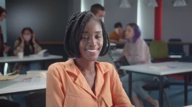 Sınıftaki masada oturan Afrikalı genç bir öğrenci kameraya bakıyor ve gülümsüyor, yavaş çekimde yakın çekim. Yüksek kaliteli FullHD görüntüler