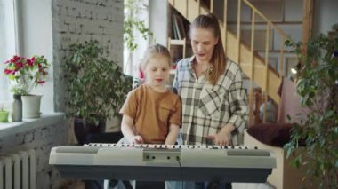 Bir müzik öğretmeni genç bir öğrenciyle ilgilenir. Kızın arkasında duruyor ve onunla birlikte sentezleyici çalıyor. Yüksek kalite 4k görüntü