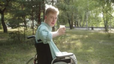 Mavi gömlekli genç bir adam içeceğini içiyor ve kameraya bakıyor ve gülümsüyor. Yüksek kalite 4k görüntü