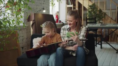  Çocuk gitar çalabilir. Telefonla müzik aleti dersi veren bir kadın. Yüksek kalite 4k görüntü