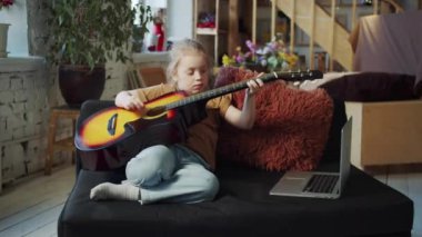 Çocuk özenle akustik gitar çalmayı öğreniyor. Gitar onun için çok büyük. Durumu iyi değil. Yüksek kalite 4k görüntü