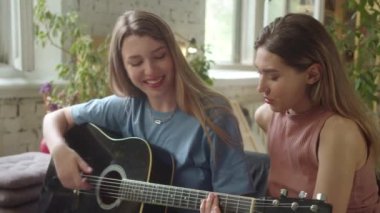 İki Igbt kızı kanepedeki astarlı odada oturmuş gitar çalıyor ve ağır çekimde şarkılar söylüyorlar. Yüksek kaliteli FullHD görüntüler