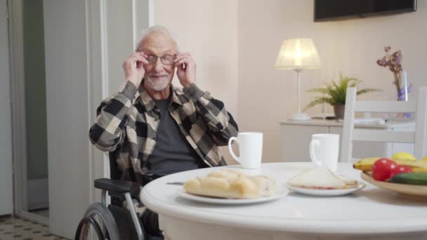 Starszy Mężczyzna Siedzi Wózku Koło Stołu Zakłada Okulary Odwraca Się — Wideo stockowe