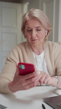 Bir emekli telefonundaki sosyal ağları araştırıyor. Kadın seviniyor ve gülümsüyor. Elinde akıllı bir saat ve masanın üstünde de güzel bir laptop var. Yüksek kaliteli FullHD görüntüler