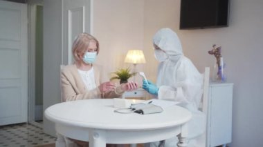 Özel kıyafetli doktor huzurevine geldi. Bir kadın ve bir hemşire masada oturuyorlar. Uzman, ısıyı özel bir aletle ölçüyor. Yüksek kalite 4k görüntü