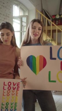 İki çekici genç kız ellerinde Igbt posterleriyle stüdyoda duruyor ve ciddi ciddi kameraya bakıyorlar. Yüksek kaliteli FullHD görüntüler