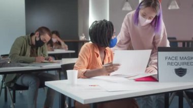 Genç profesör öğrencisinin ev ödevini kontrol ediyor ve bir sağlık çalışanı sıcaklığı ölçüyor. Yüksek kalite 4k görüntü