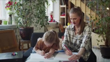 Bir kadın kanepeye oturur ve bir çocuğun resim yapmasını izler. Çizimindeki elementlere işaret ediyor ve onları övüyor yüksek kaliteli 4K görüntüler.