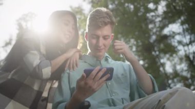 Hoş bir çift telefonda bir şey izliyor, konuşuyor ve gülümsüyor, birlikte parktalar. Yüksek kaliteli FullHD görüntüler