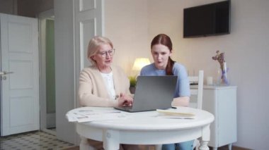 Yaşlı bir kadın ve bir kız temiz ve büyük bir dairede bir masada oturuyorlar. Laptop ekranında neler olduğunu tartışıyorlar. Yüksek kalite 4k görüntü