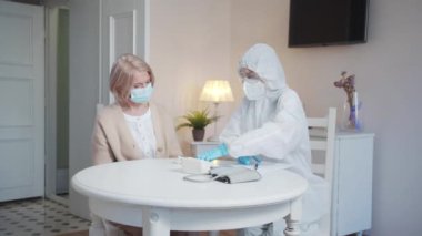 Çağrıya üniformalı bir sağlık görevlisi geldi. Termometreyle yaşlı bir kadının ateşini ölçüyor. Yüksek kalite 4k görüntü