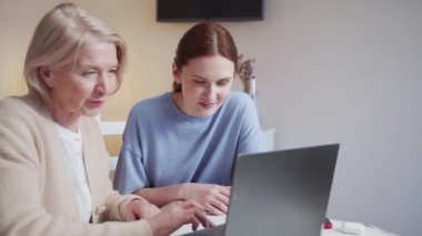 Genç bir gönüllü kız huzurevini ziyaret etti. O, yaşlı bir kadınla konuşuyor. Kız, emekliye bilgisayarın nasıl kullanılacağını açıklıyor. Yüksek kalite 4k görüntü