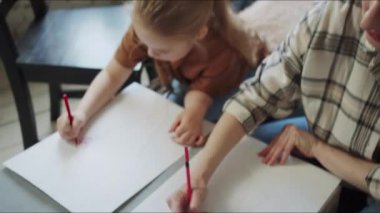 Bir kadın çocuğunun kalemle çizimini izliyor. Kız bir kalemle çizilmiş çiçekleri daire içine alıyor. Yüksek kalite 4k görüntü