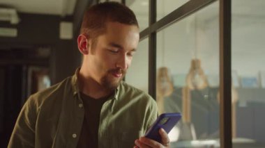 Genç bir erkek öğrenci pencerenin yanında duruyor, internette yazılar okuyor ve sonra yüzünü çeviriyor, gülümsüyor. Yüksek kaliteli FullHD görüntüler