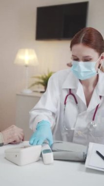 Genç bir kadın doktor termometreyle yaşlı bir adamın sıcaklığını ölçer. Sonra ona ölçü sonuçlarını gösterir. Yüksek kaliteli FullHD görüntüler