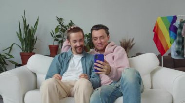 Oturma odasındaki kanepede oturan iki lgbt çekici erkek video görüşmesinde arkadaşlarıyla konuşmaya başlıyor, gülümsüyor ve sohbetin tadını çıkarıyorlar. Yüksek kalite 4k görüntü