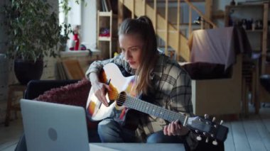 Kadın daha yeni gitar çalmaya başladı. İpleri koparıyor ve akorları sıkıyor. O, önünde duran bilgisayarda açık olan bir özel ders kullanıyor. Yüksek kalite 4k görüntü