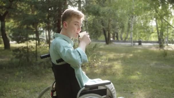 一个身穿蓝色衬衫的残疾年轻人正在喝着他的饮料 看着摄像机 面带微笑 高质量的4K镜头 — 图库视频影像
