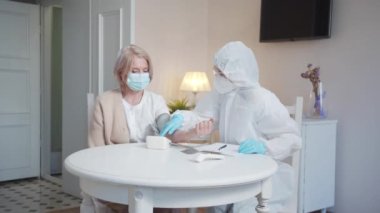  Bir kardiyolog bir büyükannenin basıncını ölçer. Doktor tonometrenin tuşlarına basar ve sonuçları bir deftere yazar.