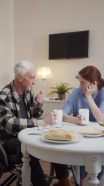 Kızı yaşlı babasını ziyaret etmeye geldi. Tekerlekli sandalyede oturuyor ve çay içiyor. Emeklilerle konuşan bir kadın. Yüksek kaliteli FullHD görüntüler