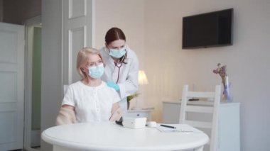 Beyaz önlüklü bir doktor yaşlı bir kadının sırtına ve göğsüne steteskop takar. Hastaların nefes alışlarını ve mırıldanmalarını dinliyor. Yüksek kalite 4k görüntü