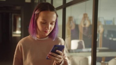 Genç bir kız öğrenci pencerenin yanında duruyor, arkadaşıyla buluşuyor ve sonra internette gülümseyen yazılar okuyor. Yüksek kaliteli FullHD görüntüler