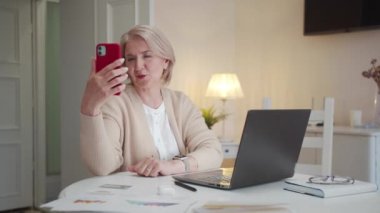 Bir büyükanne torunlarıyla video bağlantısı üzerinden konuşur. Bir elinde telefonu tutuyor ve diğer elinde çekinerek aileyi selamlıyor. Yüksek kalite 4k görüntü