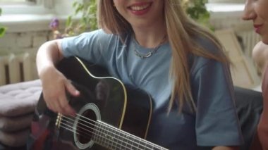 İki kız kanepede astarlı odada oturup gitar çalıyor ve ağır çekimde şarkılar söylüyor. Yüksek kaliteli FullHD görüntüler