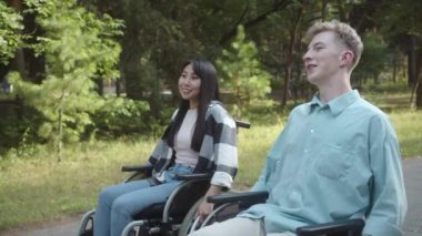 İki özürlü genç ve yakışıklı arkadaş yolda tekerlekli sandalyede yuvarlanıyorlar, konuşuyorlar ve gülümsüyorlar. Yüksek kalite 4k görüntü