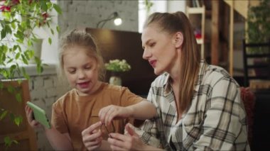 Çocuk ve ailesi kanepede otururken örülüyor. Kız annesine iplikler için yardım ediyor ve internetteki talimatlara bakıyor.