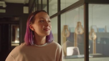 Genç bir kız öğrenci pencerenin yanında duruyor, uzağa bakıyor ve kameraya bakıp gülümsüyor. Yüksek kaliteli FullHD görüntüler