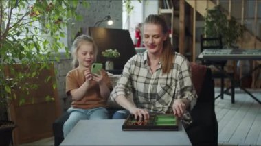 Anne ve kızı oturma odasında oturuyorlar. Çocuk telefonu kullanarak sosyal ağlarda oturuyor. Kadın satranç kutusunu açıyor. Yüksek kalite 4k görüntü