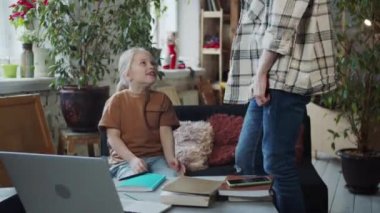 Öğretmen ve çocuk geniş bir çatı katında bir kanepede oturuyor. Masanın üzerinde kitaplar, ders kitapları ve bir dizüstü bilgisayar var. Yüksek kalite 4k görüntü