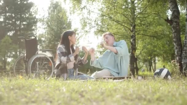一位穿着蓝色衬衫的残疾金发男子和他的黑发女友坐在格子窗上 在公园里做一些健康的锻炼 优质Fullhd影片 — 图库视频影像