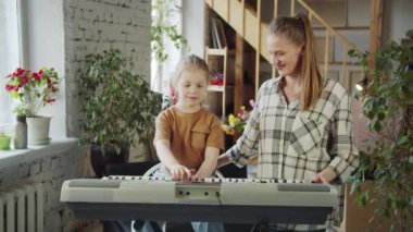 Çocuk öğretmenle birlikte elektronik piyano çalar. Kadın dikkatle kızların maçını izliyor ve sonunda onu övüyor. Yüksek kalite 4k görüntü