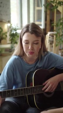 İki Igbt kızı kanepede oturmuş gitar çalıyor ve şarkılar söylüyorlar. Yüksek kaliteli FullHD görüntüler