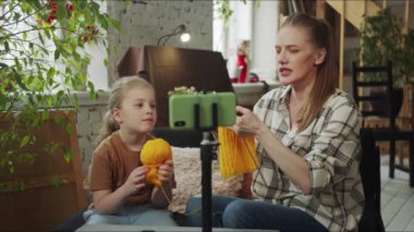 Çocuk ve anne siyah bir kanepede oturup örgü örüyorlar. Önlerindeki masada tripodun üzerinde bir telefon var ve video çekiyor. Yüksek kalite 4k görüntü