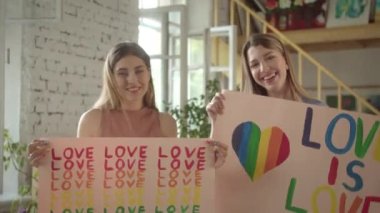 İki çekici genç kız ellerinde Igbt posterleriyle stüdyoda duruyorlar ve kameraya bakıp gülümsüyorlar. Yüksek kaliteli FullHD görüntüler