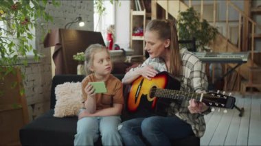 Bir kadın gitar çalmayı öğreniyor. Kızı bir telefon tutuyor ve annesine notlar gösteriyor. Yüksek kalite 4k görüntü