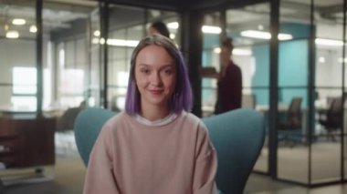 A young extraordinary cute student sits on the armchair in the university and looks at the camera seriously, slow motion. High quality 4k footage