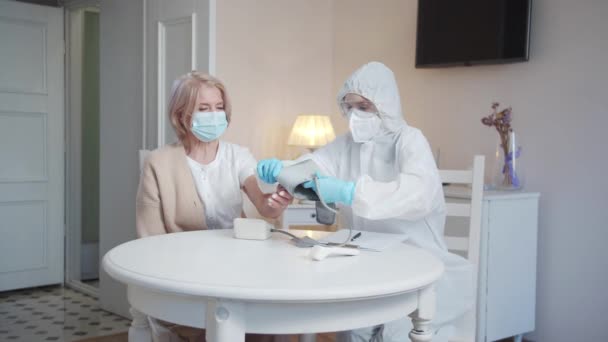 防護服を着た女性とマスクは 高齢者の女性の手にクロノメータースリーブを置き 測定を開始します 高品質4K映像 — ストック動画
