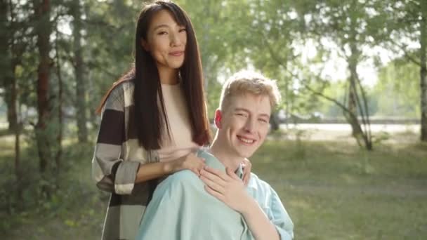一位有着一头长长的黑头发的年轻的亚洲女人正在抚摸着她穿着蓝色衬衫的残疾年轻人 她们看着相机笑着 高质量的4K镜头 — 图库视频影像