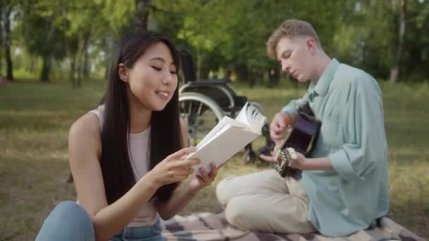Молодая Симпатичная Азиатка Сидит Клетке Просматривает Книгу Пока Парень Инвалид — стоковое видео