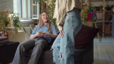 A young pretty lady sits on the sofa in the living room, then she meets her best friend and they star talking to each other. High quality 4k footage