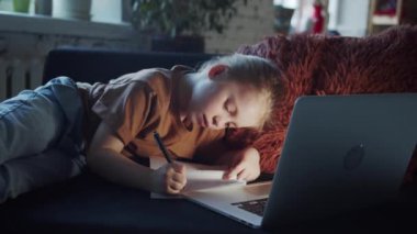 The schoolgirl does homework at night. She writes with a pen in her notebook. She looks at the computer screen. High quality 4k footage