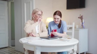 Kız, gözlüklü büyükannesiyle birlikte internette resimlere göz atıyor. Telefonu kullanırlar. Eğlenceli ve mutlular. Gülüyorlar, gülüyorlar. Yüksek kalite 4k görüntü