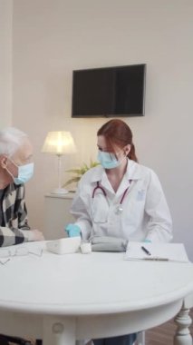  A doctor in a medical mask and gown communicates with an elderly patient in a wheelchair and gives him advice. High quality FullHD footage