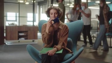 A young student-girl with curly hair is removing protective face mask her face mask, looking at the camera smiling, slow motion. High quality 4k footage