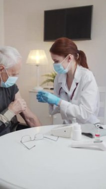 A woman doctor wipes a mans shoulder with a cotton swab with alcohol. She then injects the vaccine with a syringe. High quality FullHD footage