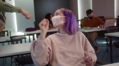 An attractive guy-student is coming into the classroom, greeting his classmates and sitting down his desk. High quality 4k footage